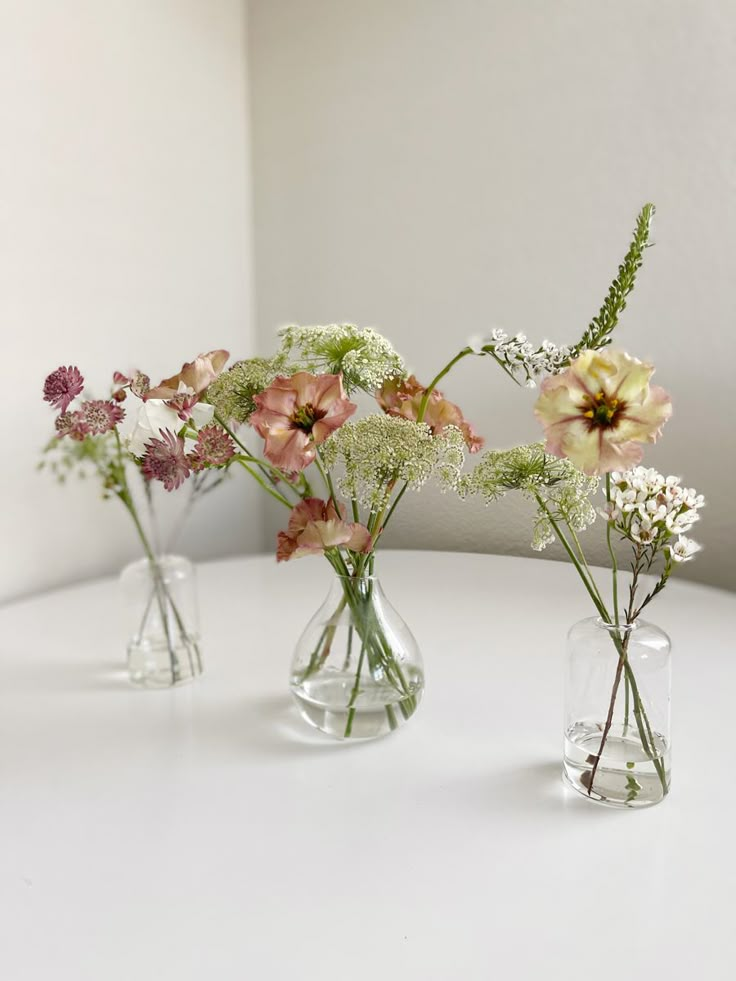 three glass vases with flowers in them on a table