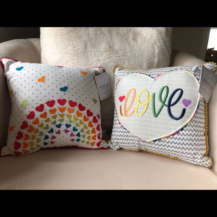 two pillows with the word love on them sitting on a couch in front of a white pillow