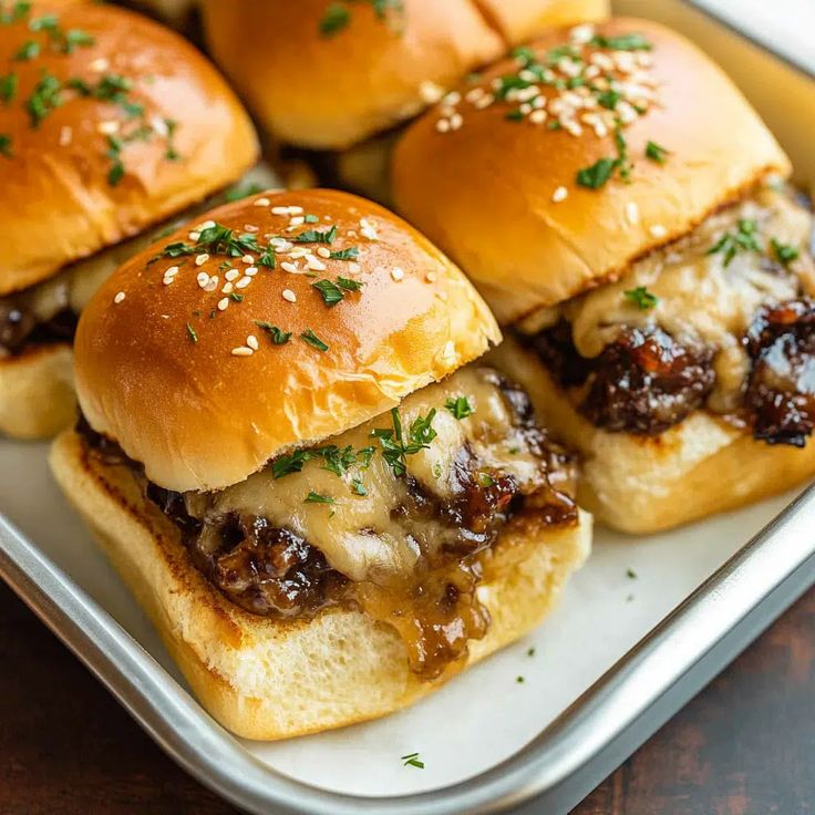 several sliders with meat and cheese are on a white plate, ready to be eaten