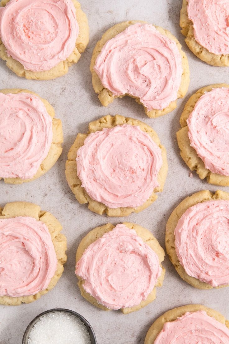 cookies with pink frosting are arranged on a baking sheet