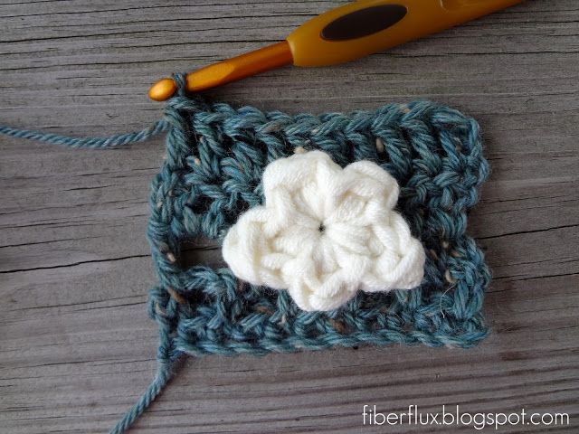 a crocheted square with a white flower on it next to a pair of scissors