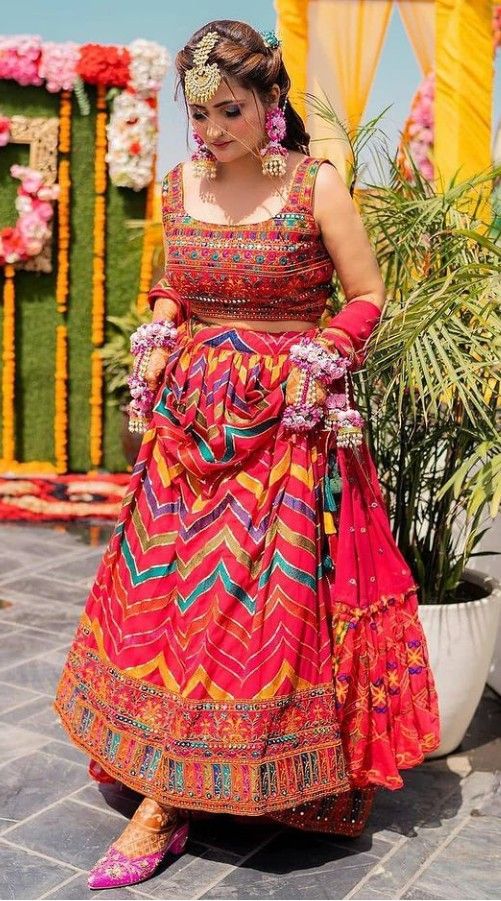 a woman in a colorful dress and headpiece is standing on the ground near flowers