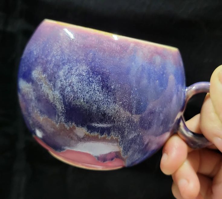 a hand holding a purple and blue coffee mug with white speckles on it