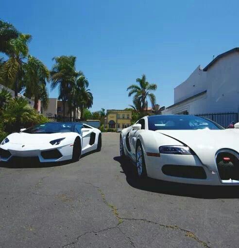 two white sports cars parked next to each other in front of a building with palm trees