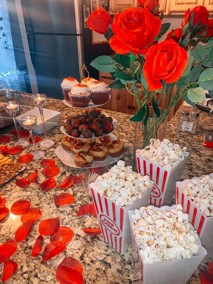 a table topped with lots of food next to red roses and cupcakes on top of a counter