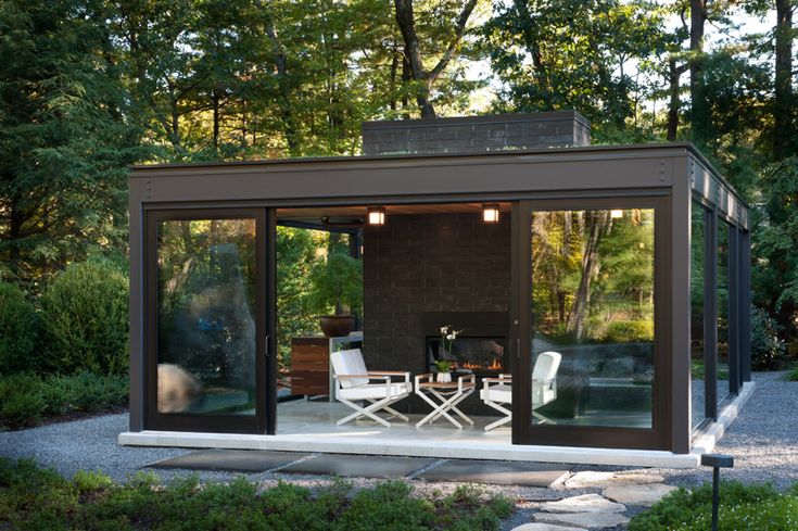 a small house in the middle of some grass and trees with two chairs on it