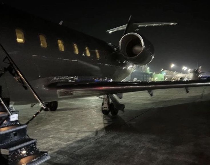 an airplane sitting on the tarmac at night with its lights on and stairs leading up to it