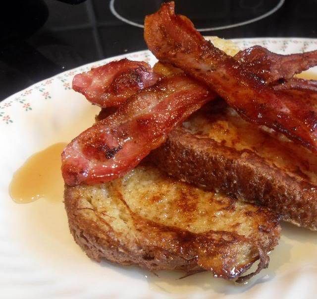 two pieces of bacon on top of french toast sitting on a plate with syrup drizzled around it