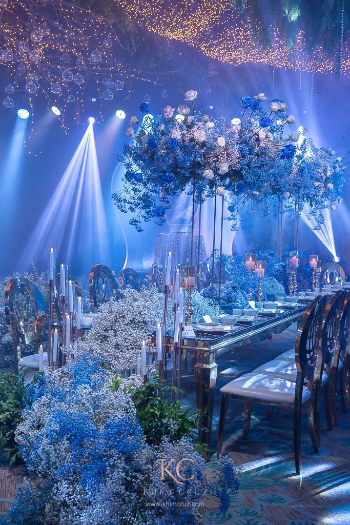 an elaborately decorated dining room with blue lighting and flowers on the table, surrounded by tall trees