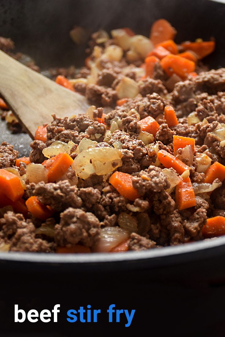 beef and carrots cooking in a skillet with a wooden spoon on the side