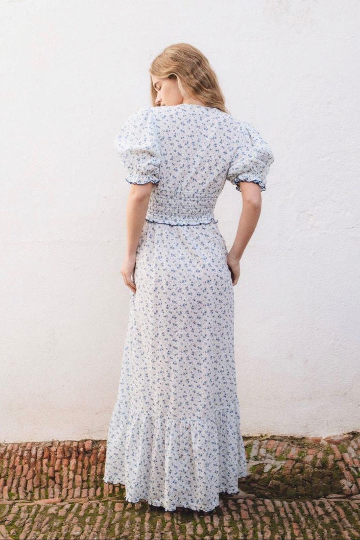 Our India floral print dress is a long dress inspired from the Edwardian era made in a delicate organic cotton voile. It features V-neck and so many feminine details. Its stretchy smocked bodice finishes with a delicate crochet trimming, and gives way to a full-length skirt with in a big ruffle at the bottom. Color: blue 100% cotton Maxi length BSCI certified. Made in India. Fitted V-neck Dress With Smocked Cuffs, Summer Prairie Dress With Smocked Bodice For Gatherings, Spring Smock Fitted Maxi Dress, Spring Fitted Smock Maxi Dress, Fitted V-neck Peasant Dress, Fitted Smocked Dress With Maxi Length And Smocked Cuffs, Fitted Smocked Maxi Dress With Smocked Cuffs, Fitted Blue V-neck Smocked Dress, Blue Fitted V-neck Smocked Dress