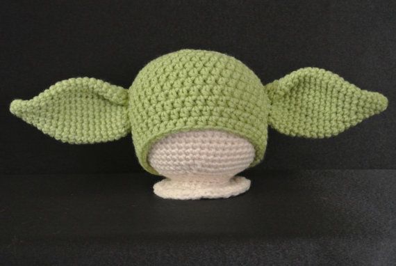 a green knitted yoda hat sitting on top of a black table next to a pink flower