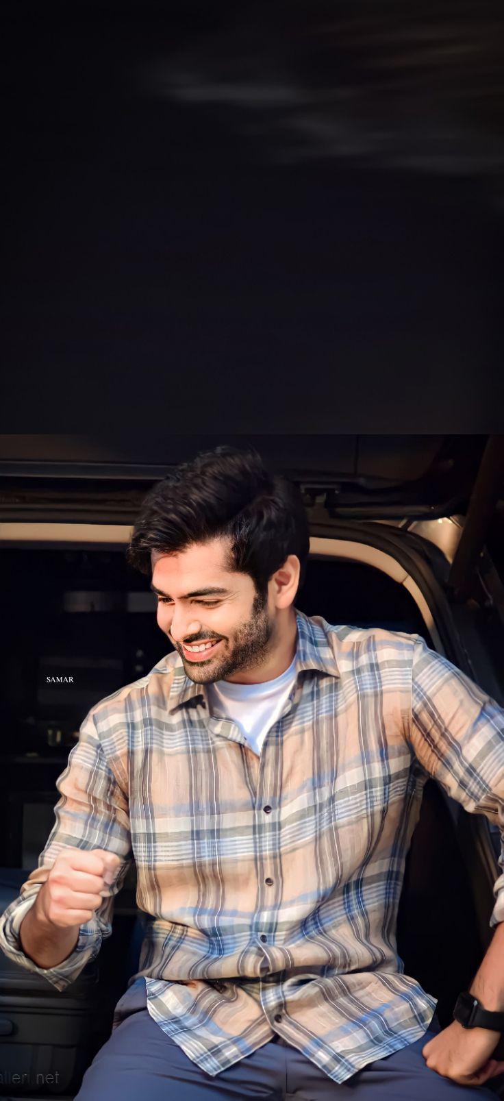 a man sitting in the back of a car with his hand on his hip and smiling