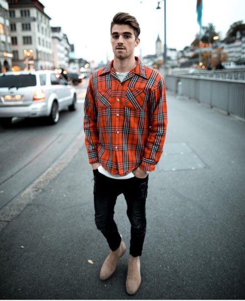 a man standing on the side of a road wearing an orange shirt and black pants