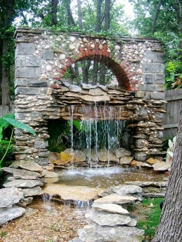 a small waterfall in the middle of a stone wall with an arched window above it