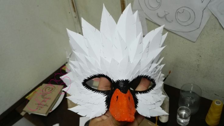 a person is holding up a paper mask with an orange beak and white feathers on it