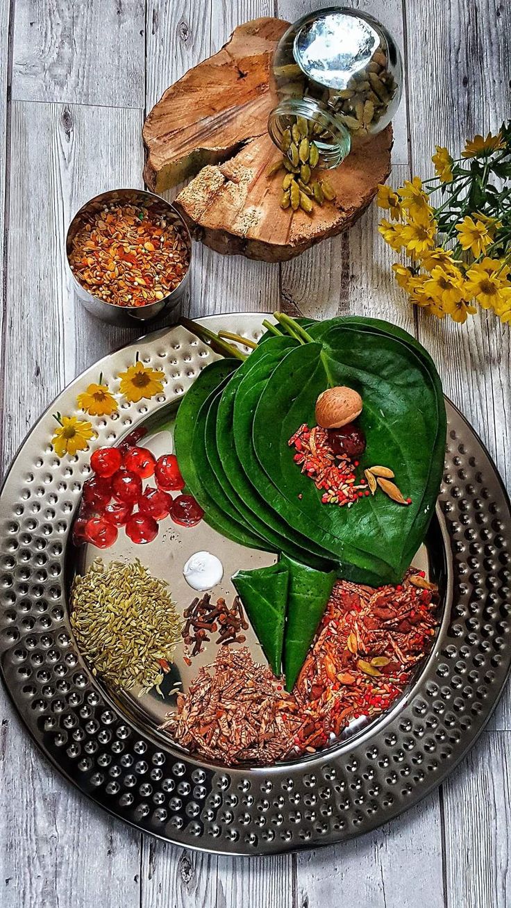 an assortment of spices and herbs on a metal platter next to other dishes with flowers