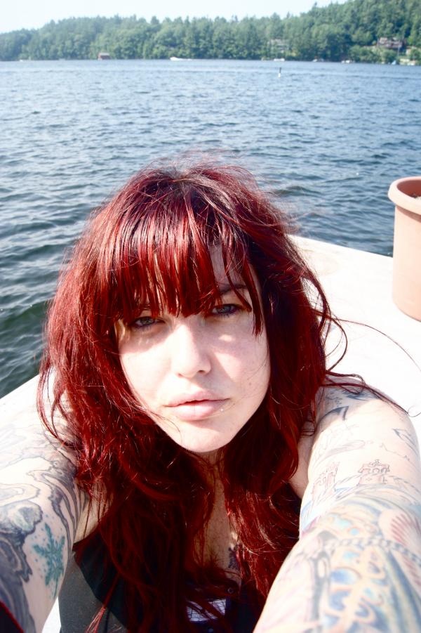 a woman with red hair and tattoos on her arm sitting in a boat looking at the camera