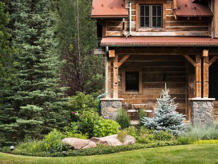 a log cabin sits in the middle of a lush green yard with rocks and trees