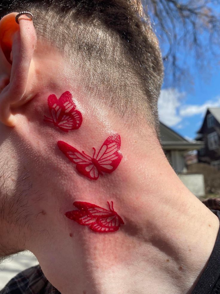 a man with three red butterflies on his neck and behind his ear, in front of a blue sky