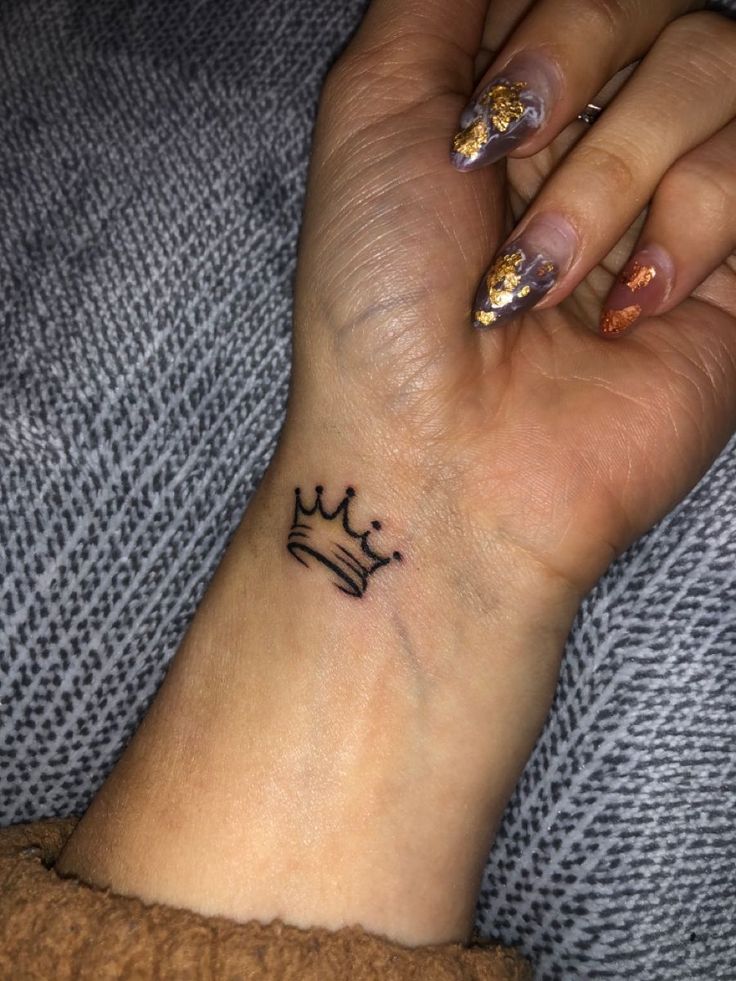 a woman's wrist with a crown tattoo on it