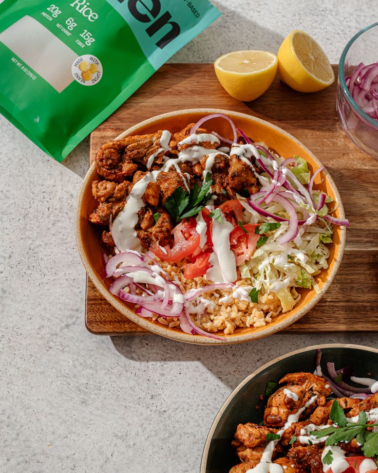 two bowls filled with food sitting on top of a wooden cutting board next to a bag of rice