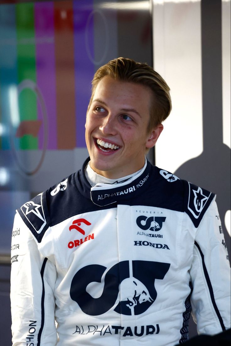 a man in a white and black racing suit smiles at the camera while sitting down