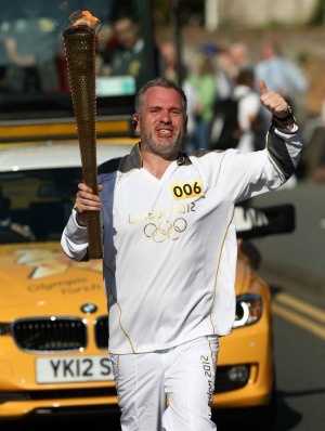 a man in white is walking down the street holding a pole and wearing an olympic outfit