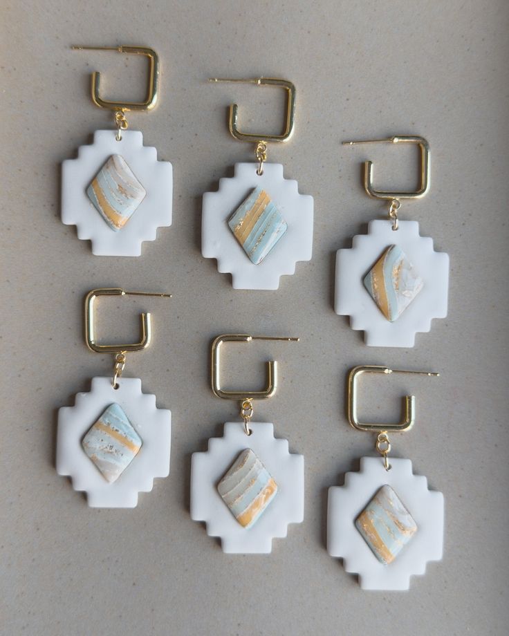 six pieces of white and gold jewelry on a gray surface with clippings attached to them