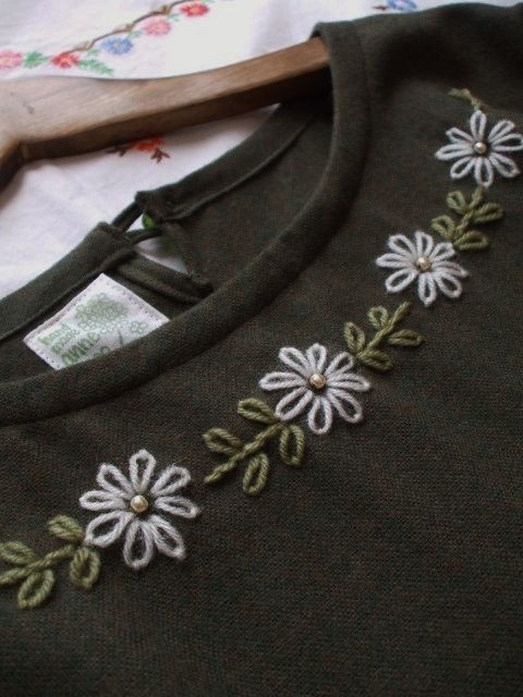 a green sweater with white flowers on it and a wooden hanger next to it