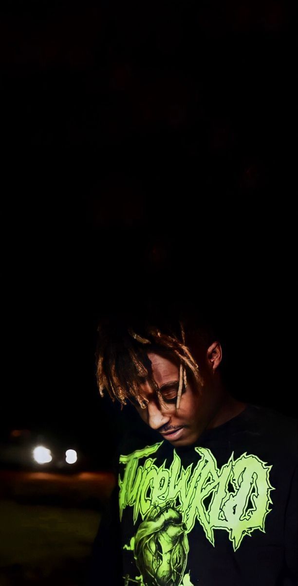 a young man with dreadlocks standing in the dark looking at his cell phone