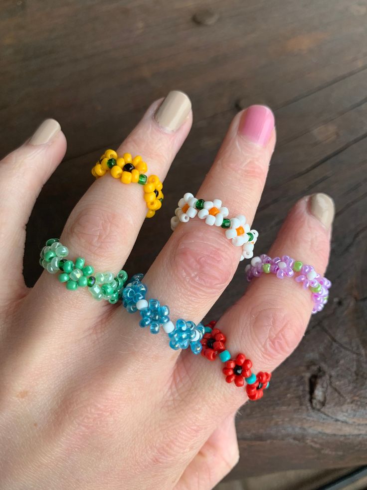 a woman's hand with four different colored beaded rings on her thumb and fingers