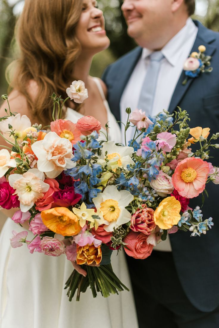 a bride and groom smile at each other as they hold a large bouquet of flowers