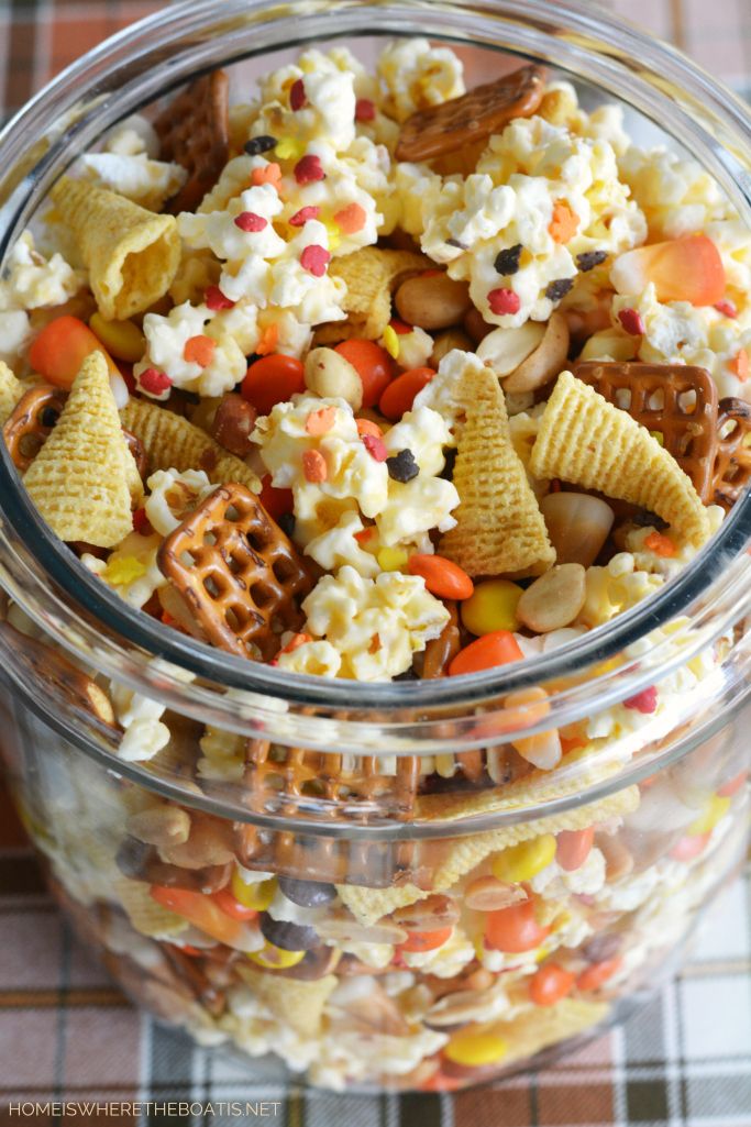 a glass jar filled with candy corn and cheetos popcorn mix on a checkered table cloth