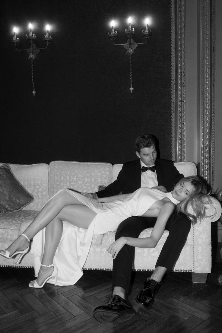 a man and woman sitting on top of a couch in front of chandeliers