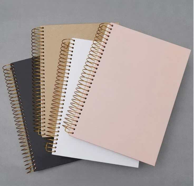 four spiral notebooks lined up next to each other on top of a gray surface