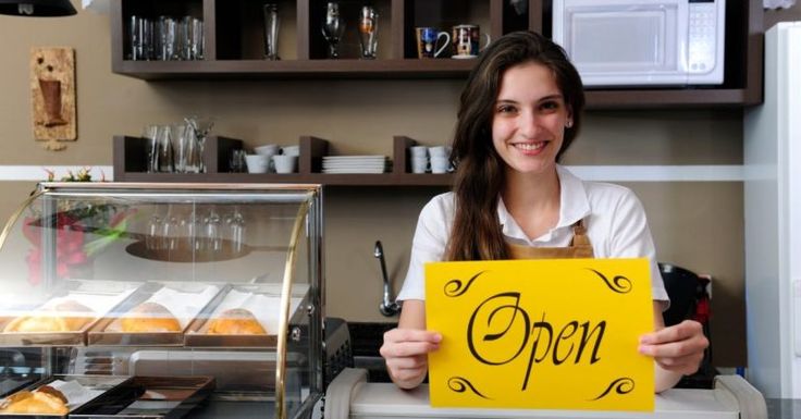 a woman holding up a sign that says open in front of a counter with pastries