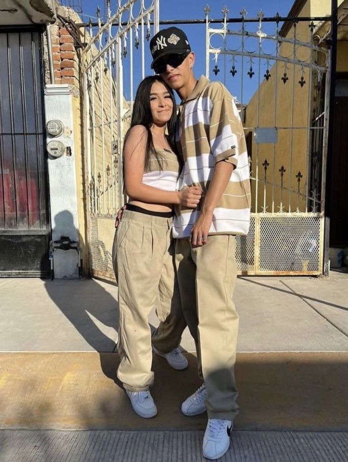 a man and woman standing next to each other in front of a gated area