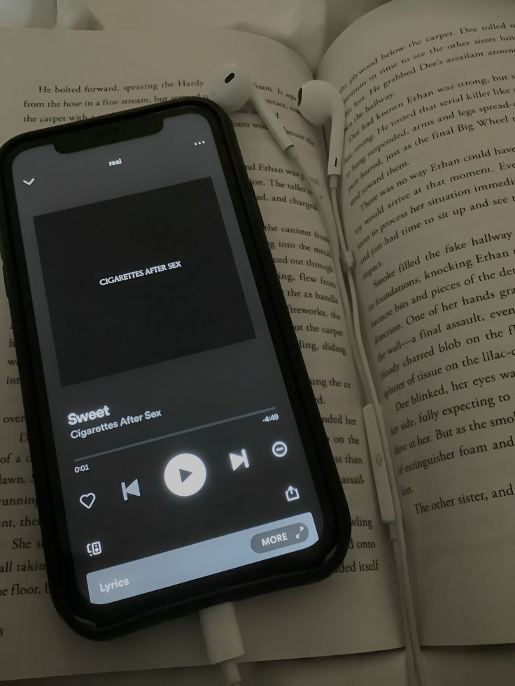 an open book with headphones on top of it next to a cell phone that is plugged in