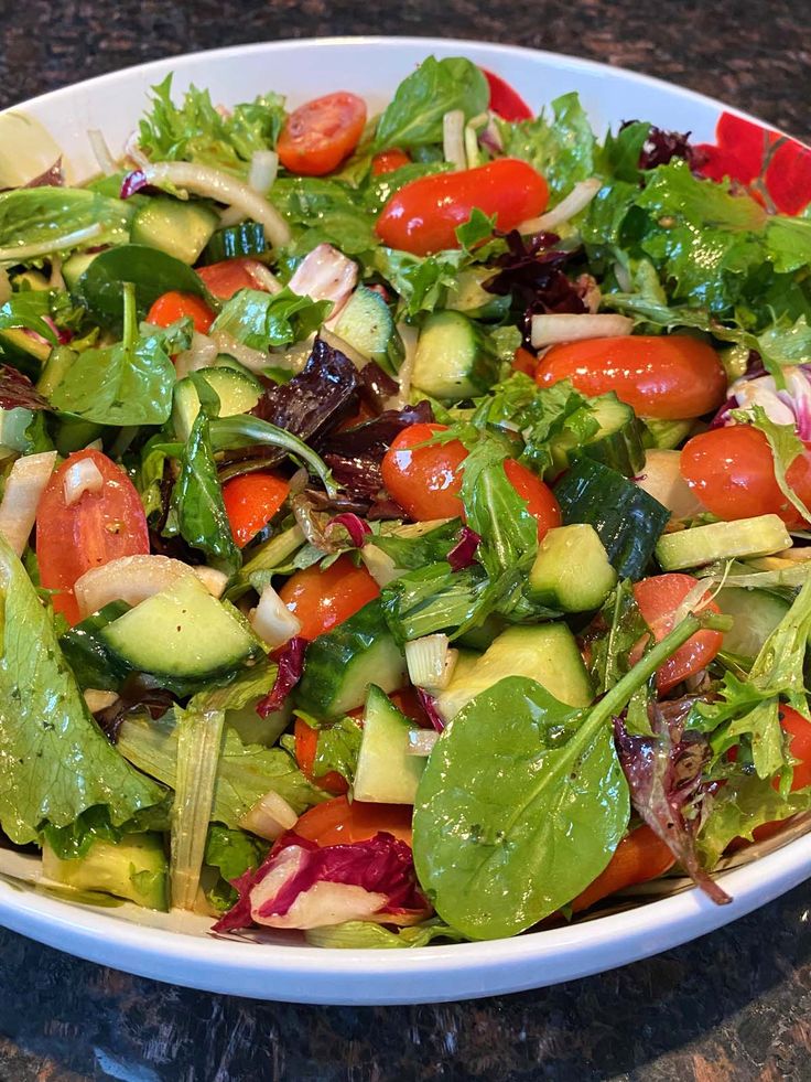 a salad with tomatoes, lettuce and cucumbers in a white bowl