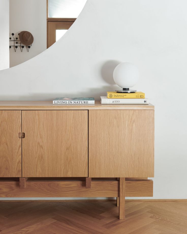 a wooden sideboard with books on top and a mirror above it in a white room