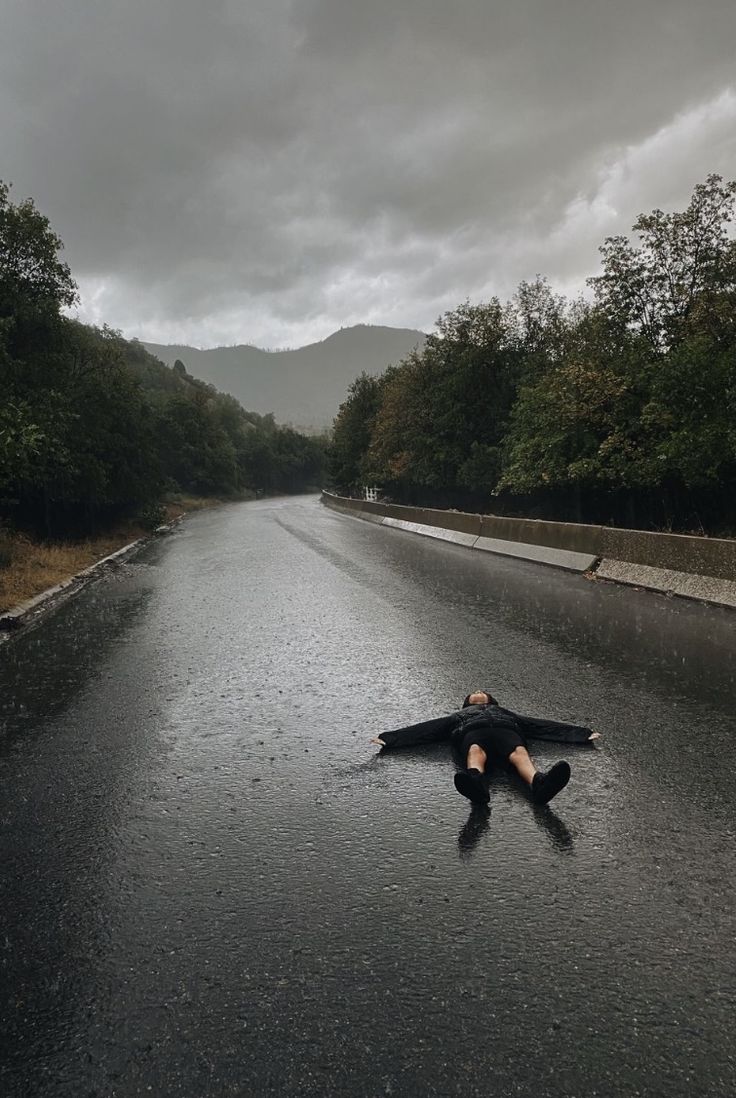 a man laying on the side of a wet road in the middle of the day