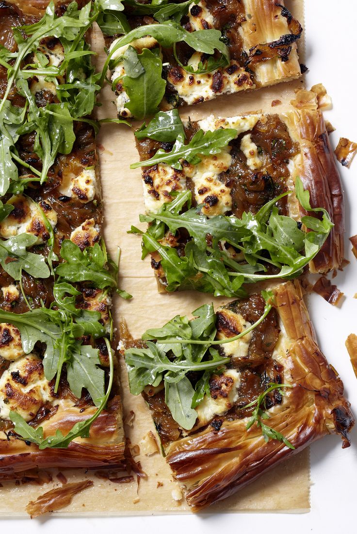 a pizza topped with lots of greens on top of a wooden cutting board next to other food items