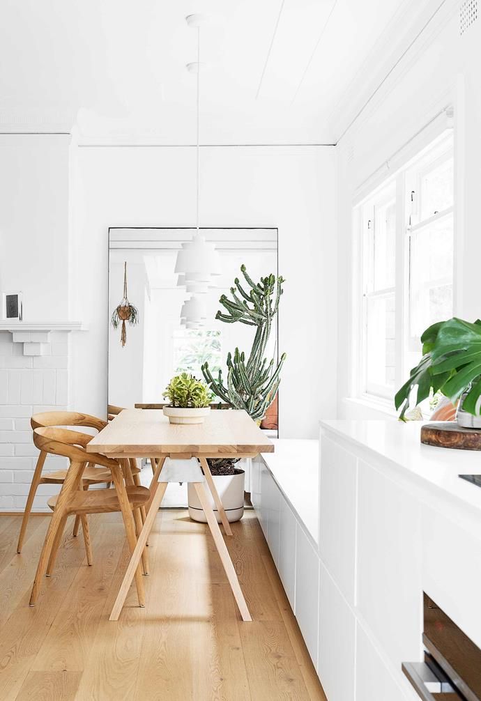 a kitchen with white walls and wooden floors, along with a dining table surrounded by chairs