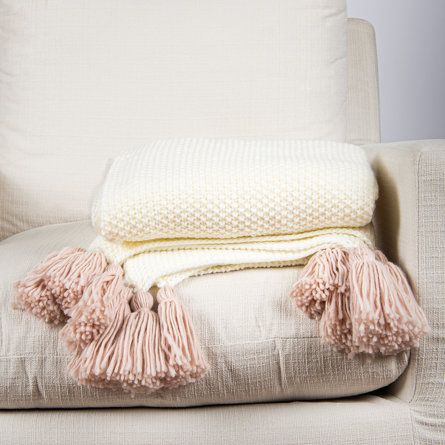 a white chair with two blankets on top of it and a pink throw pillow next to it