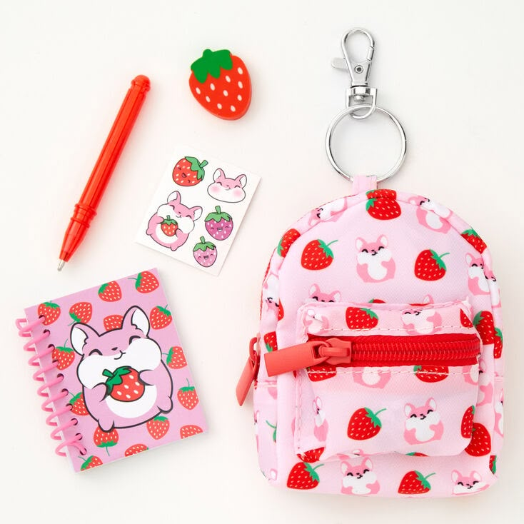 a pink backpack with strawberries on it next to a notepad, pen and keychain