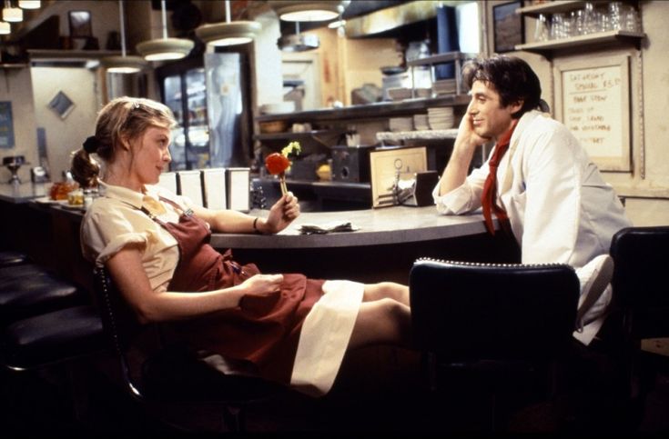 a man and woman sitting at a bar with one holding a rose in his hand