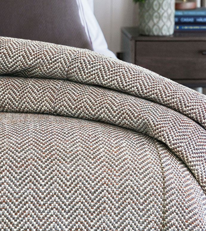 a bed with a brown and white comforter next to a night stand