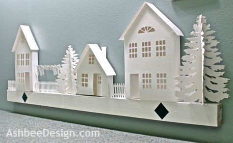 a white paper cutout of houses and trees on a shelf next to a green wall