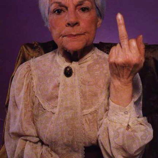 an older woman sitting in a chair making the peace sign with her hand and wearing a white blouse